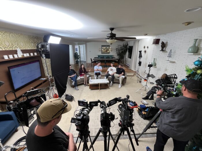 A video production team aims cameras at subjects on a couch